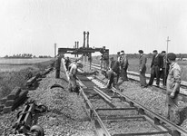 834491 Afbeelding van wegwerkers van de N.S. tijdens het leggen van stukken spoor met betonnen dwarsliggers met behulp ...